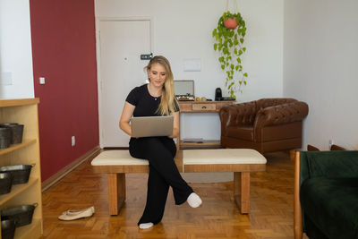 Woman working at home from couch with laptop on her lap. home office concept. gray notebook