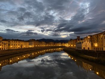 Illuminated buildings by river against sky at dusk