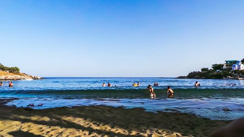 People enjoying at beach against clear blue sky