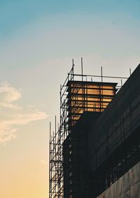 Low angle view of silhouette crane by building against sky during sunset