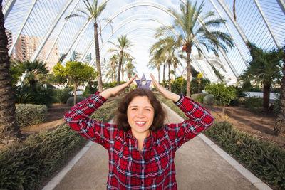 Portrait of smiling young woman standing against palm trees