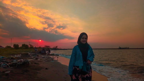 Young woman standing on beach against sky during sunset