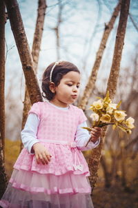 Cute girl holding flower while standing against trees in forest