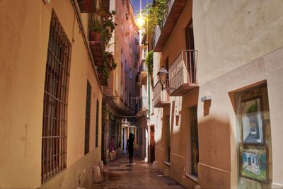 Rear view silhouette woman walking in narrow alley amidst buildings