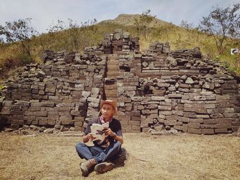 Full length of a man sitting on stone wall