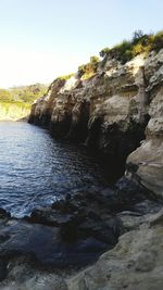 Rock formation by river against sky