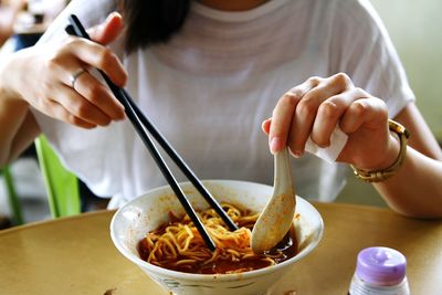 Midsection of woman holding chopsticks and spoon over hokkien mee bowl