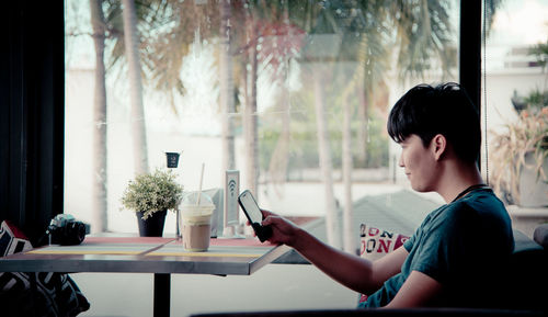 Side view of man using mobile phone while sitting on table