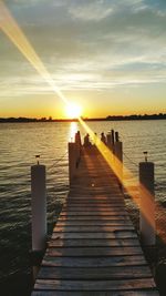 People sitting at wooden pier during sunset