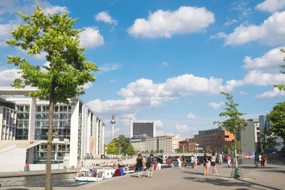 People walking by canal in city against sky