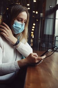 Woman wearing mask using mobile phone in cafe