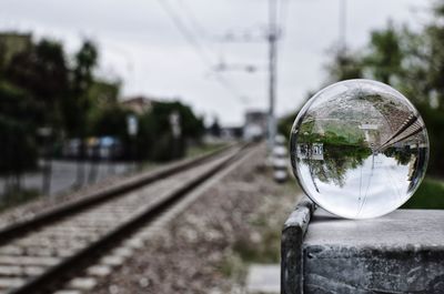 Close-up of crystal ball by railroad tracks against sky
