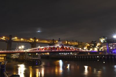 Illuminated bridge over river against sky at night