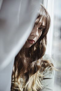 Portrait of woman hiding behind window curtain