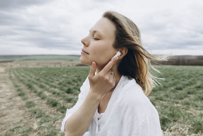 Woman with eyes closed adjusting in-ear headphones at agricultural field