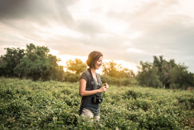 Woman standing amidst plants against sky during sunset