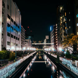 Light trails on road by illuminated city against sky at night