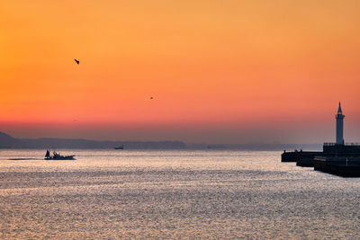 Silhouette birds flying over sea against orange sky