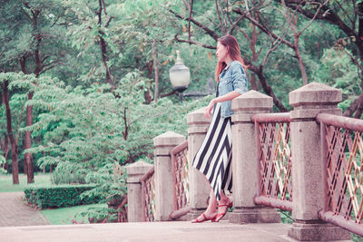 Woman sitting on bench against trees