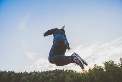 Low angle view of man jumping against blue sky