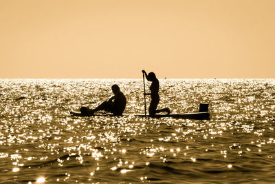 Silhouette people on sea against clear sky during sunset