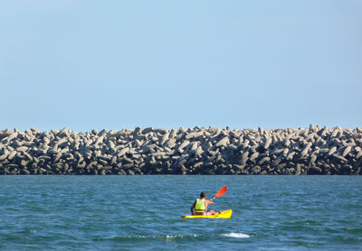 Man on rock by sea against clear sky