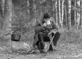 Black and white photo of a forester by the fire, man drinking tea, blurred forest background, wild