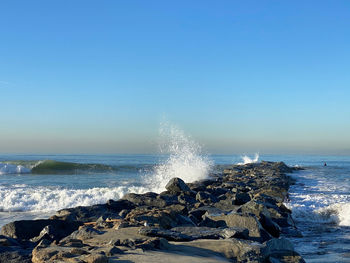 Sea waves splashing on rocks against clear sky