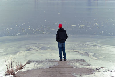 Rear view of man standing in sea during winter