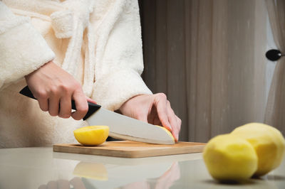 Woman in bathrobe cutting raw peeled potatoes on cutting wooden board at home kitchen