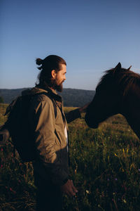 Side view of man touching horse on field