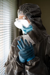 Woman wearing protective suit and mask standing by window