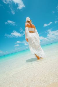 Rear view of woman standing at beach against sky