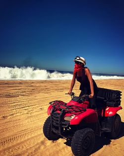 Woman riding quadbike while covering face with scarf on sand at beach during sunny day