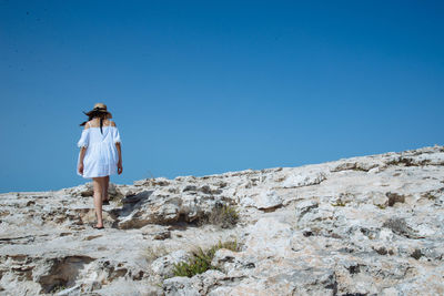 Rear view of woman walking on rock formation against clear sky