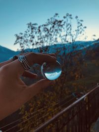 Cropped hand of woman holding crystal ball against mountains during sunset