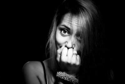 Portrait of smiling woman with hand covering mouth against black background