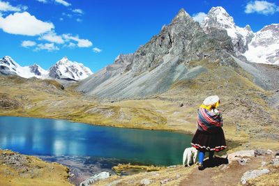 Rear view of woman standing on rocky mountain against sky