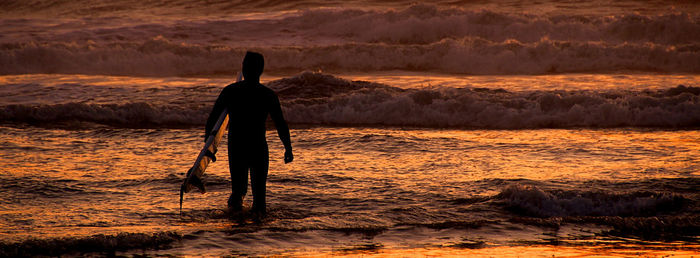 One more wave. the fiery sun  sets on the lone surfer as night envelopes all. serenity.