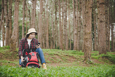 Woman sitting on dirt road amidst trees in forest