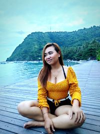 Beautiful young woman sitting against mountains and sky