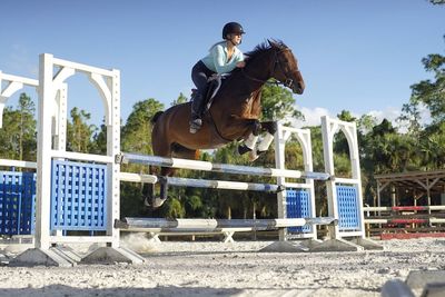 Young woman on horse crossing obstacle at field