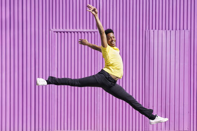 Smiling man with arms raised jumping in front of cabin