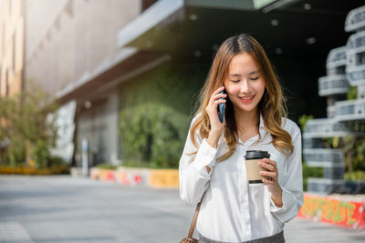 Young woman using mobile phone while standing in city