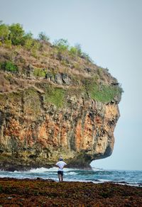 Rear view of woman standing on cliff by sea against clear sky