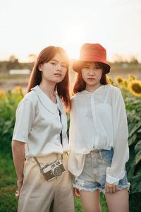 Portrait of female friends standing at sunflower farm during sunset