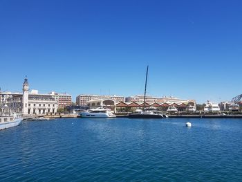 Sailboats in sea by buildings against clear blue sky