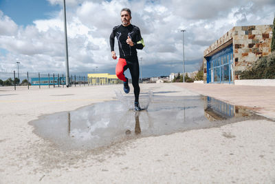 Mature man jogging on road against cloudy sky