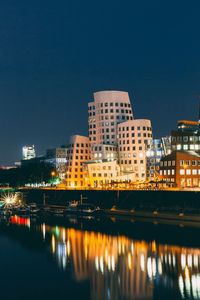 Illuminated buildings by river against sky at night