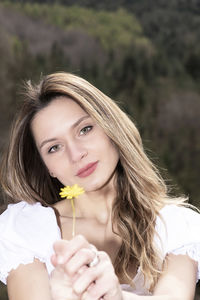 Blonde woman dressed in white offering a flower to camera